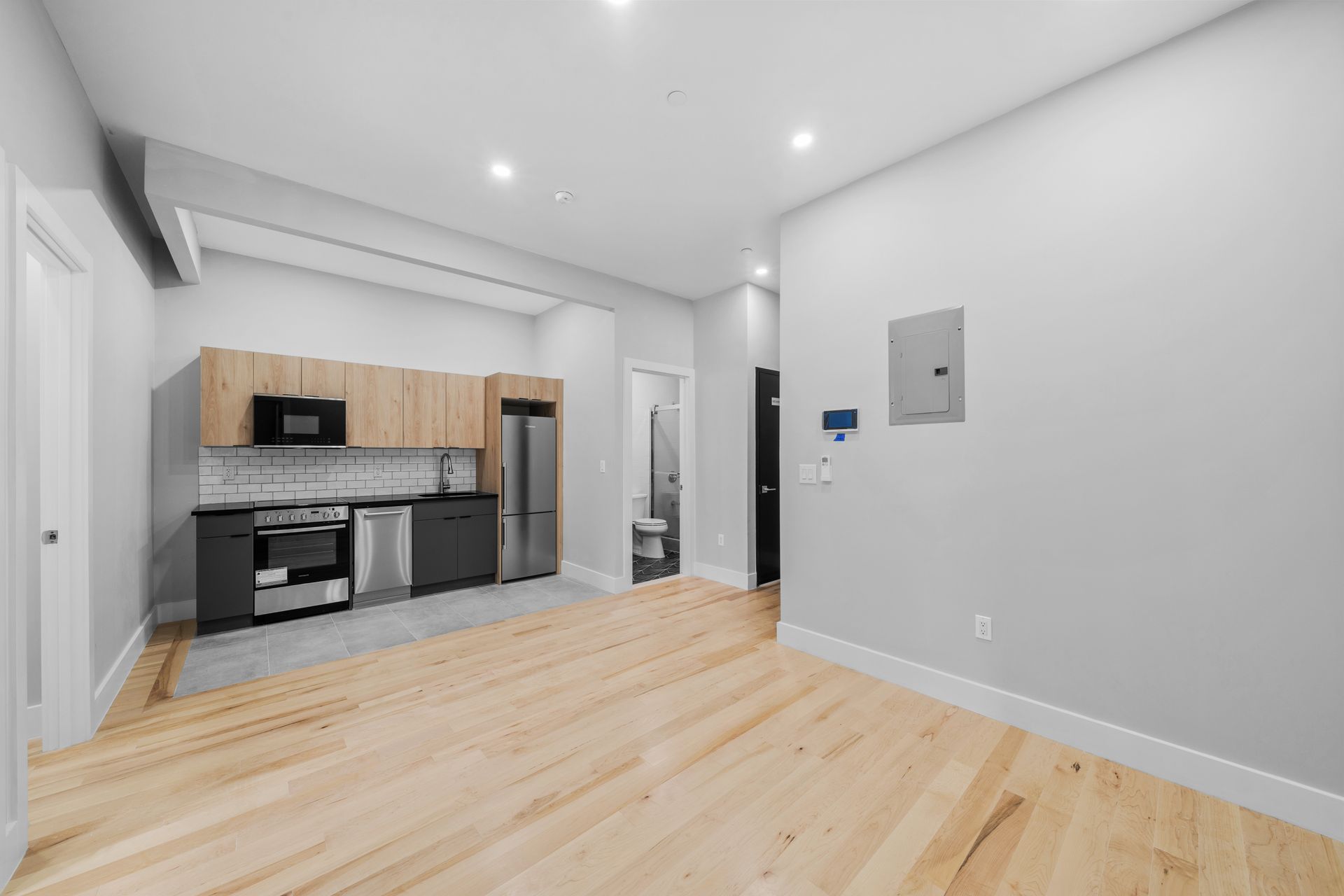 A living room with hardwood floors and a kitchen with stainless steel appliances.