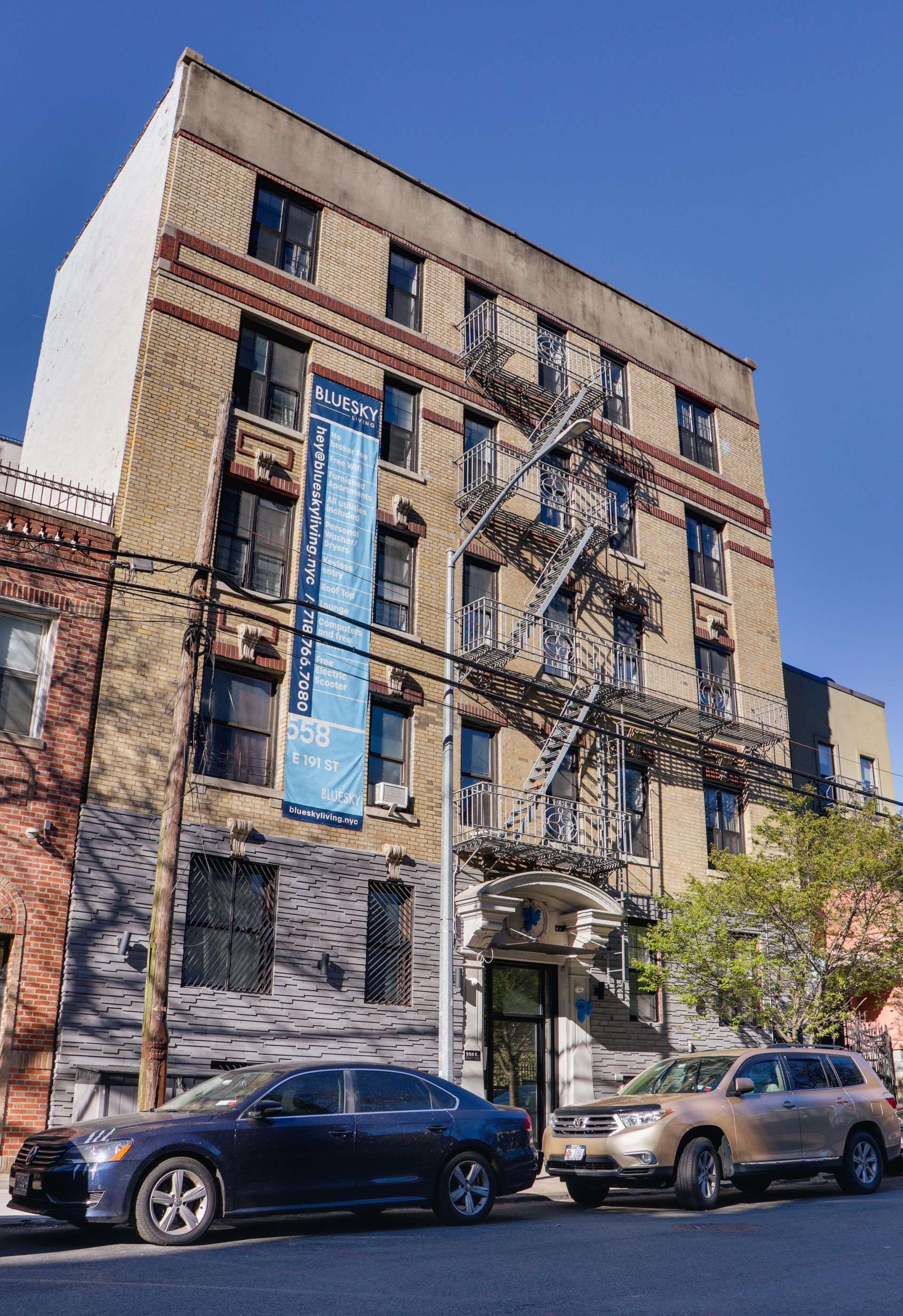 Two cars are parked in front of a building with a fire escape.