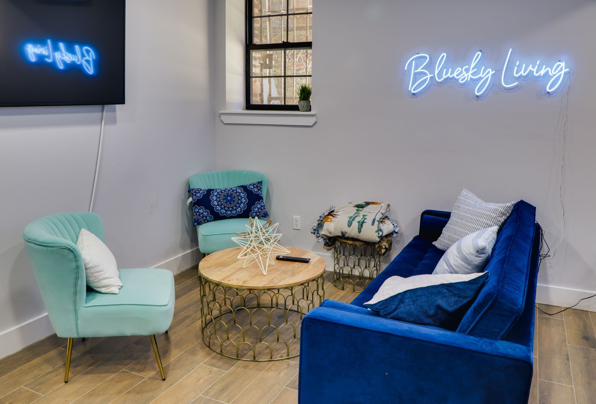 A living room with a blue couch , chairs , and a neon sign.