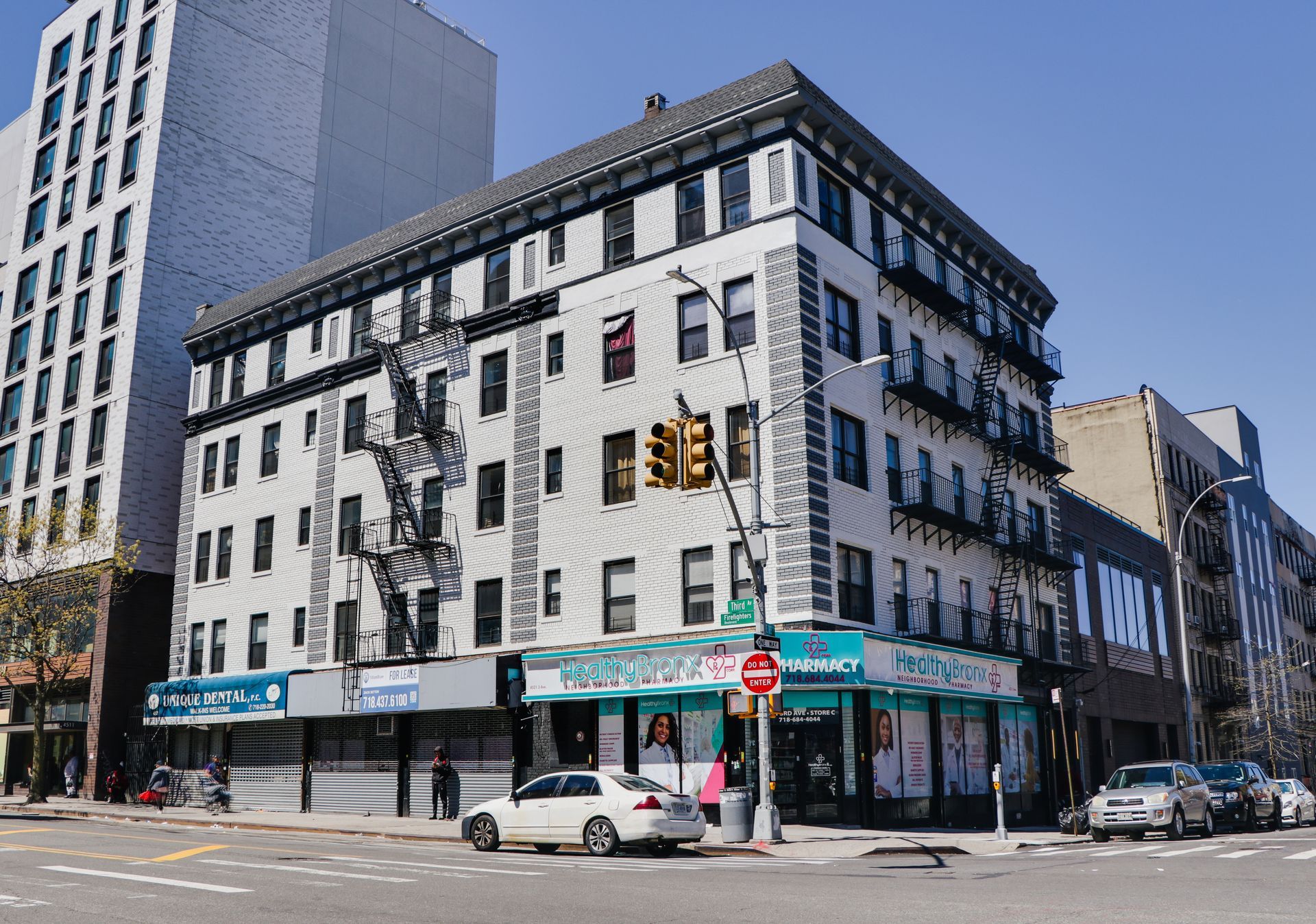 A white car is parked in front of a building on the corner of a city street.