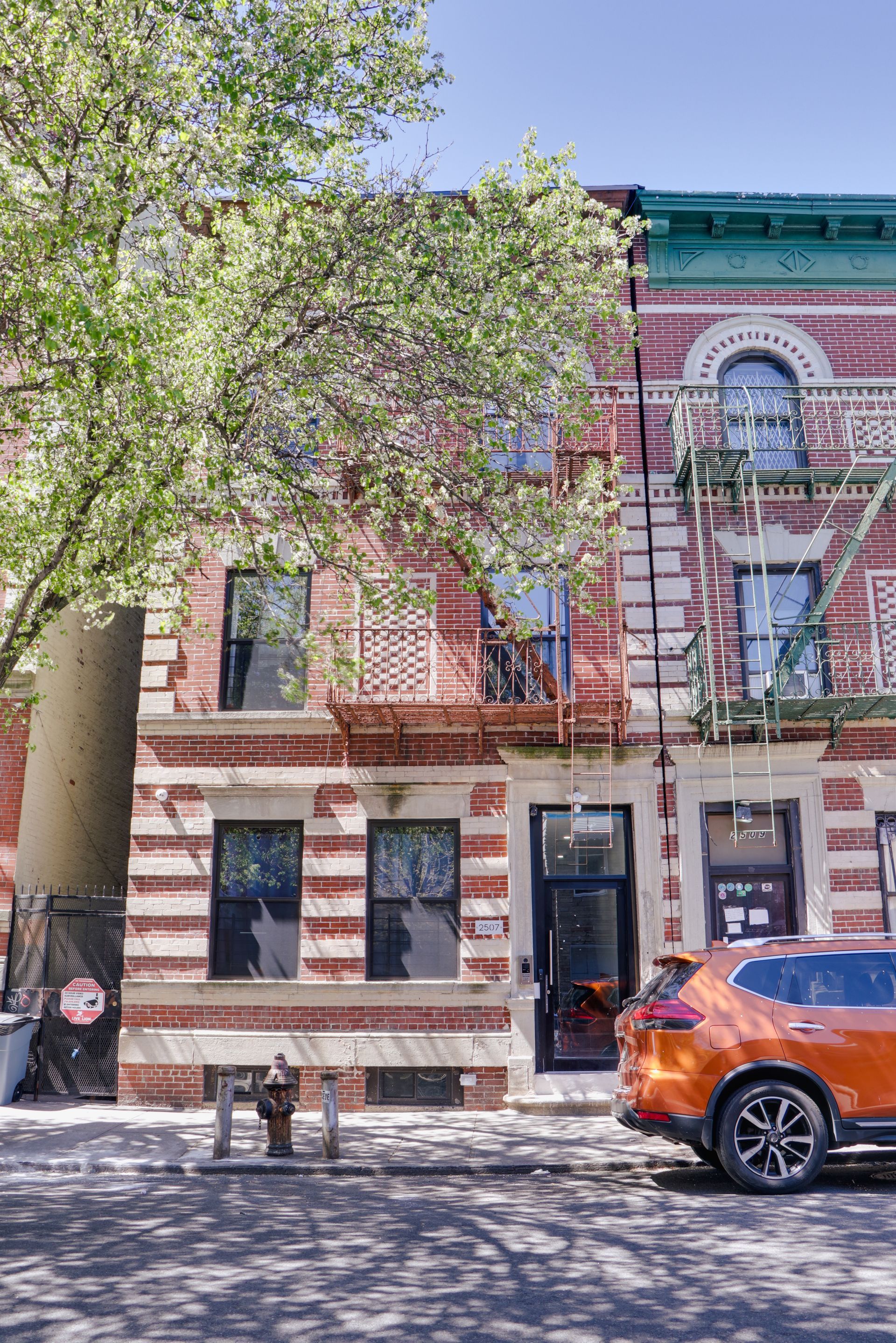 A car is parked in front of a brick building with a fire escape.
