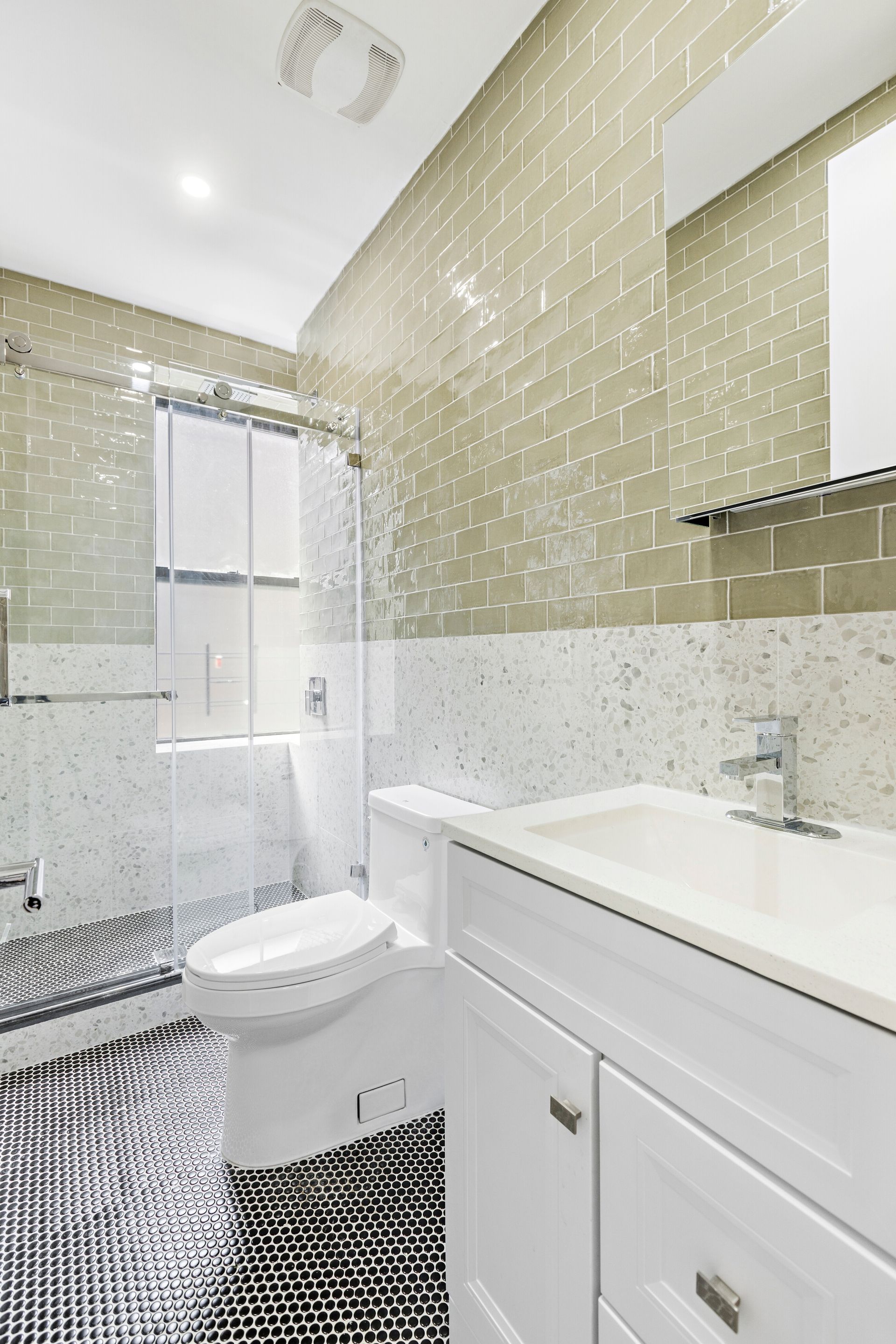 A bathroom with a toilet , sink , mirror and shower.