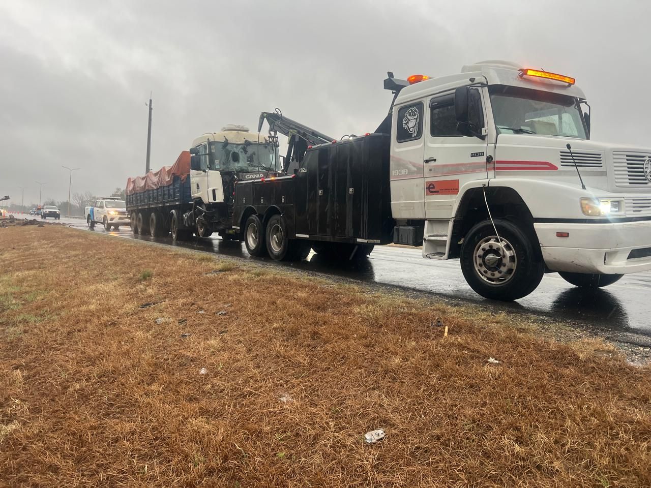 Un gran camión grúa transportando equipo pesado por una carretera mojada bajo un cielo nublado.