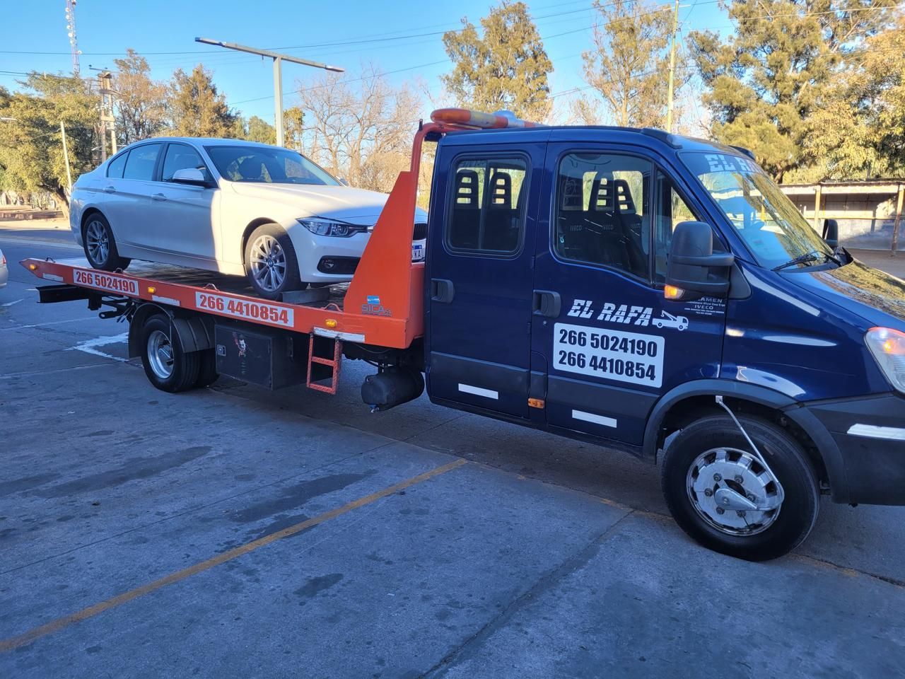 Grúa remolcando un coche blanco sobre una plataforma, estacionado en un aparcamiento.