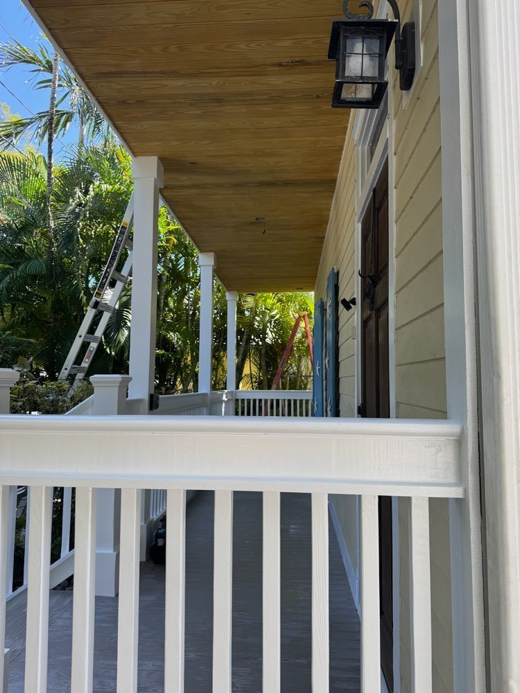 A porch with a wooden ceiling and a white railing on a house.