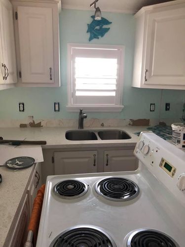 A kitchen with a stove , sink , cabinets and a window.