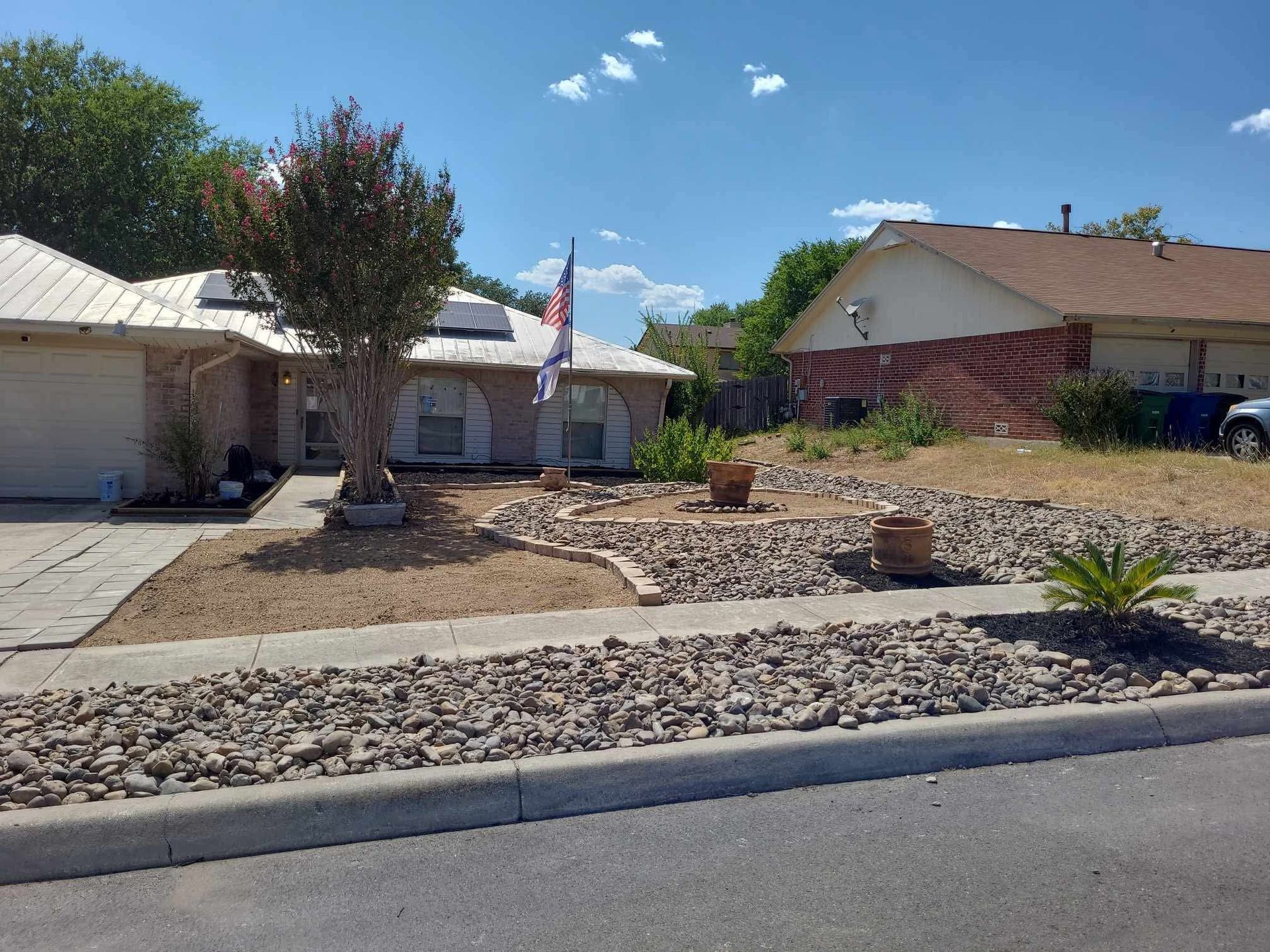 Suburban front yard with desert landscaping, single-story homes, and an American flag under a blue sky