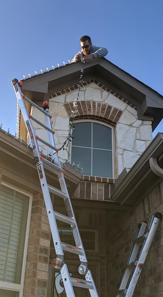 Man on a roof beside a ladder, working above a house with a large arched window.