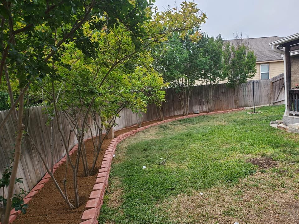 Backyard with green lawn, small trees, and a wooden fence curving along a brick border