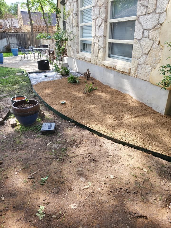 Stone house exterior with a fresh dirt planting bed and potted plants along the wall.