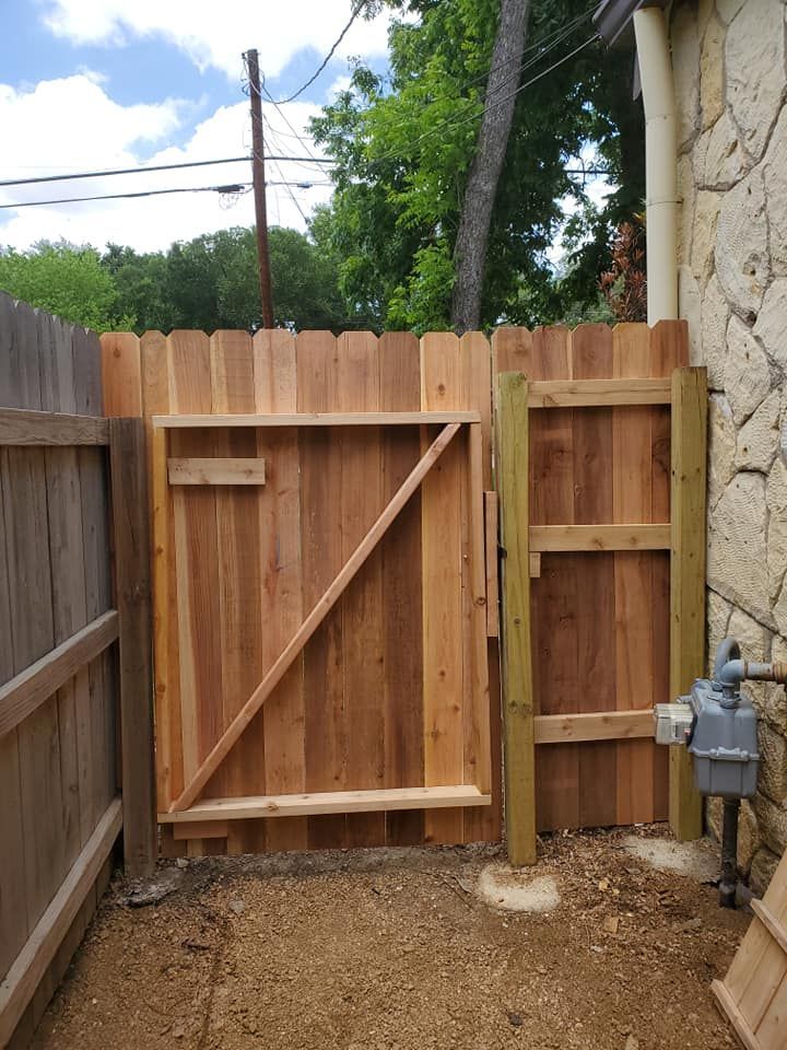 Wooden backyard gate with diagonal brace between a fence and a house wall, over dirt ground.