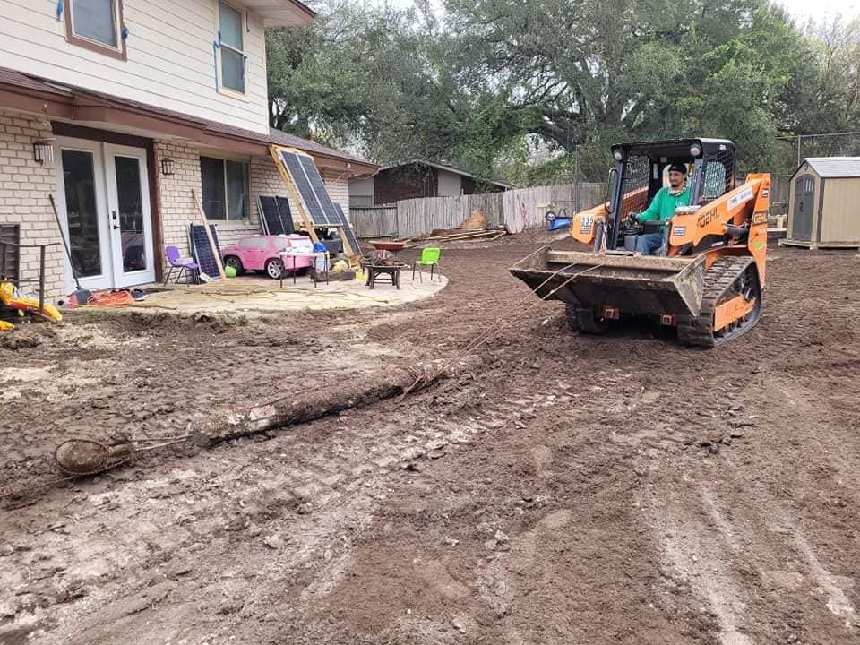 Construction equipment and workers grading a muddy driveway beside a house