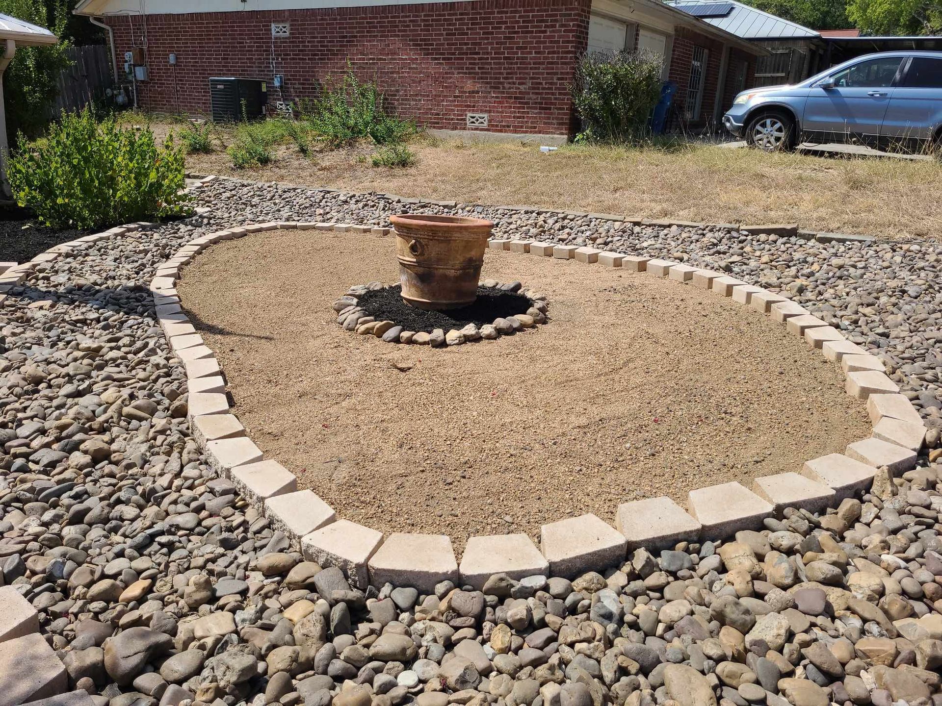 Backyard rock garden with circular gravel bed, stone border, and a small planter in the center.