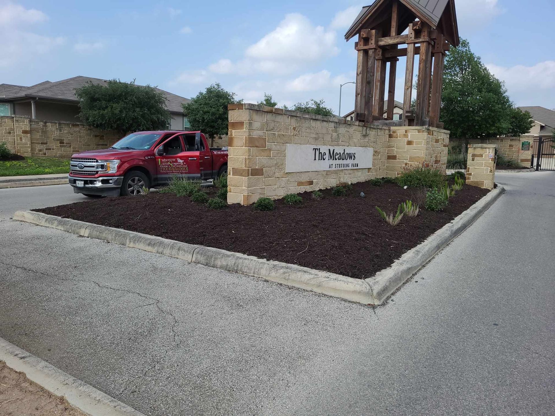 Red pickup truck by a stone entrance sign and wooden pavilion at a neighborhood entrance