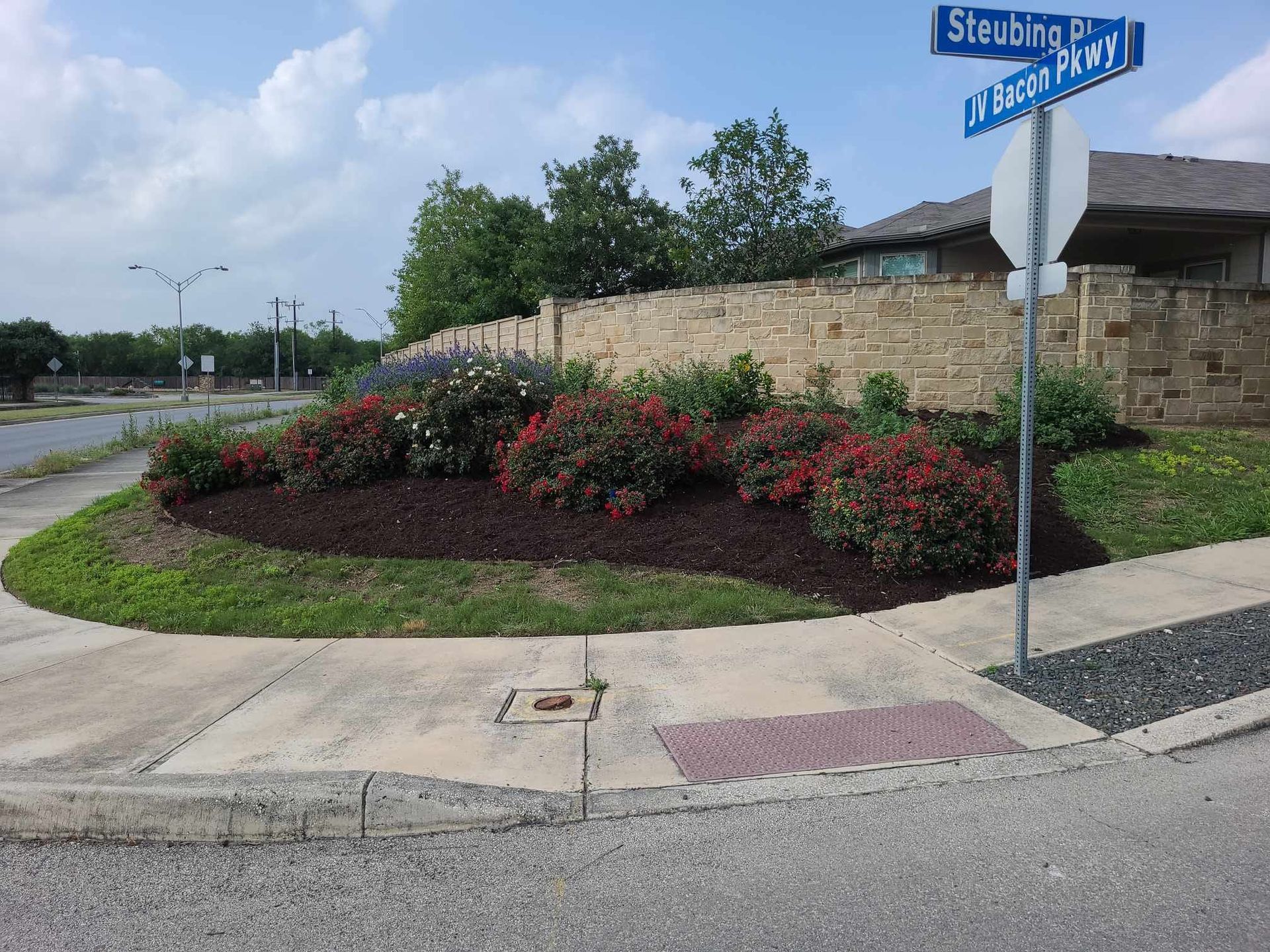 Street corner with landscaped flower bed and stone sign near a driveway under cloudy sky