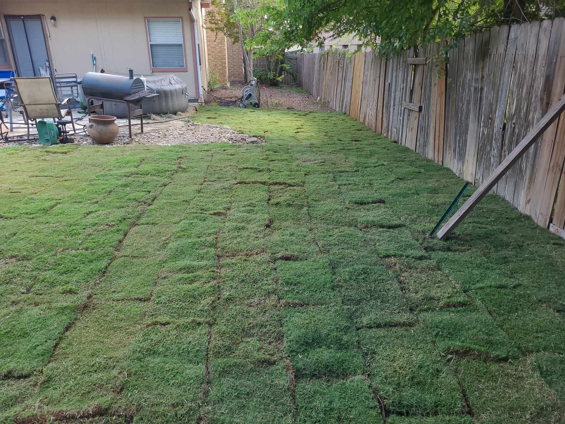 Backyard with a worn grassy path beside a wooden fence and a patio area near a house