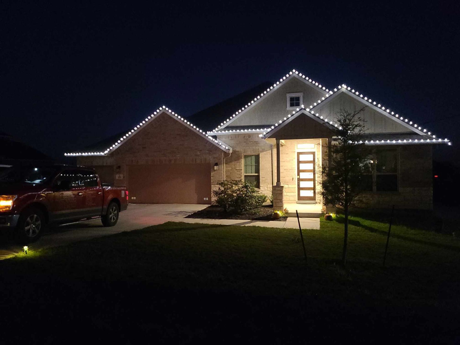 Suburban house at night with white roof lights and a lit front door, red truck parked in driveway