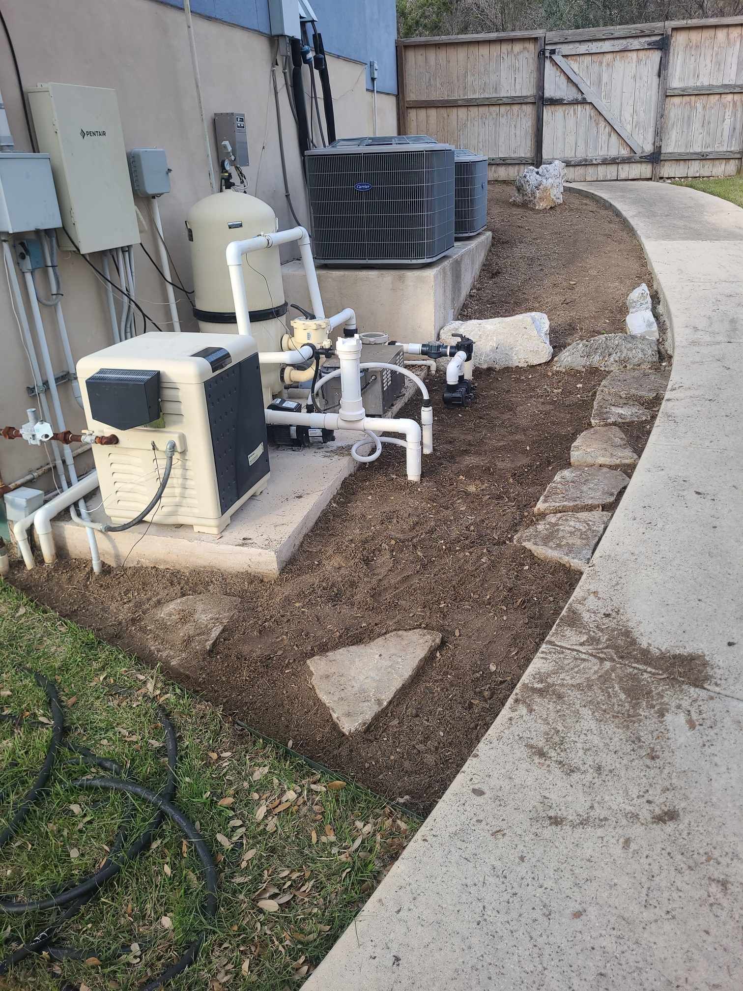 Outdoor HVAC equipment and pipes beside a building, with a curved concrete path and gravel area