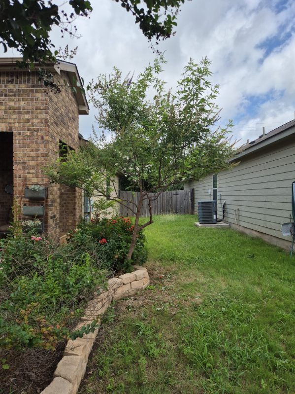 Backyard with a tree, grassy lawn, brick house on the left, and gray-sided house on the right.