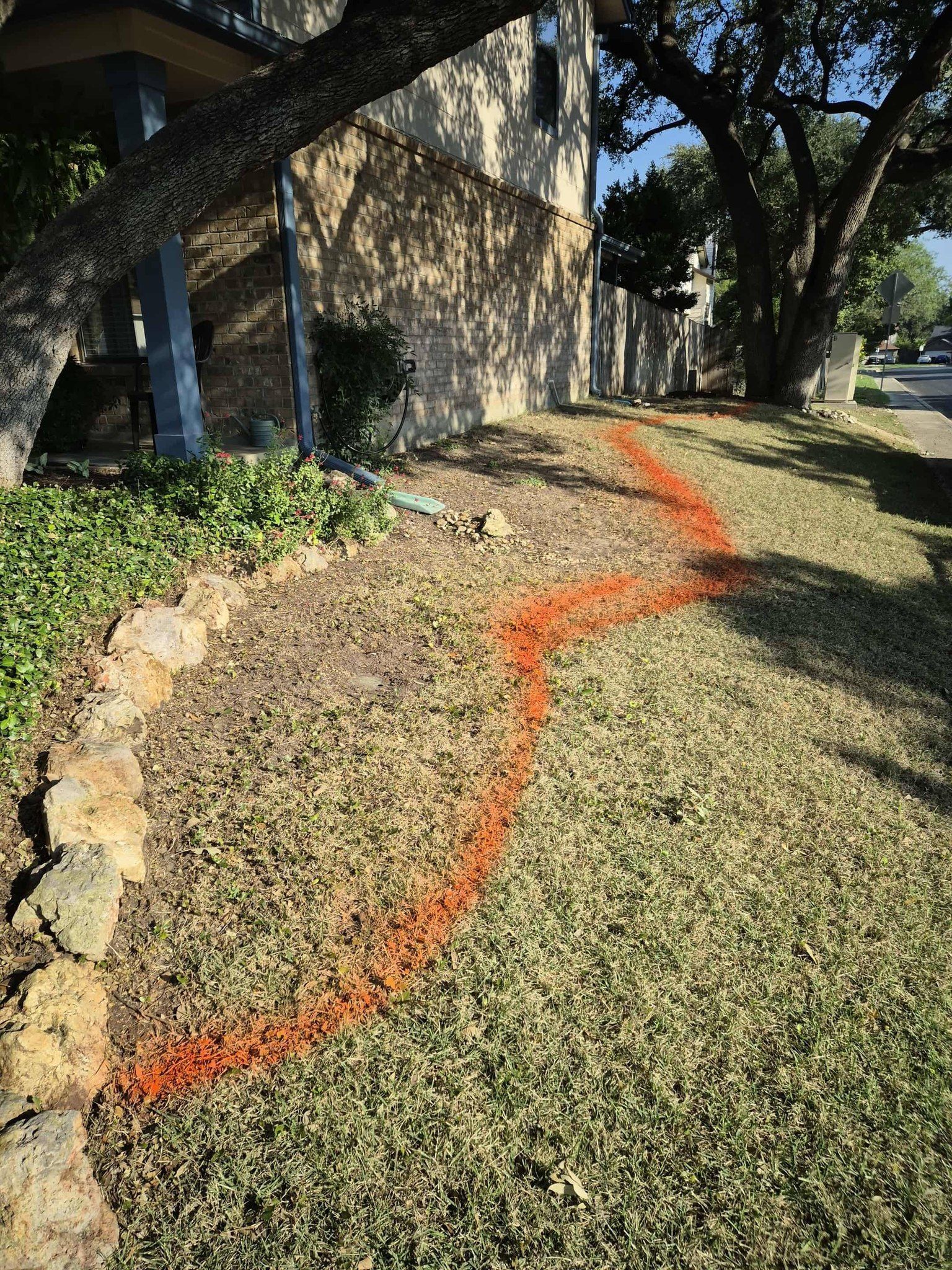 Front yard sloped lawn with an orange marking, beside a stone house and trees.