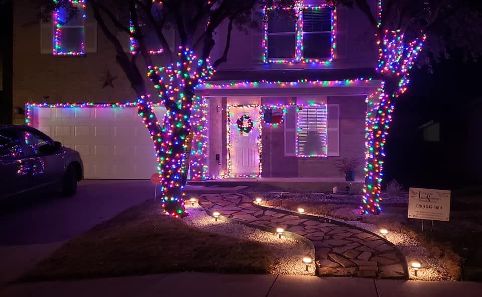 House decorated with colorful Christmas lights at night, with a lit tree and garage in the background