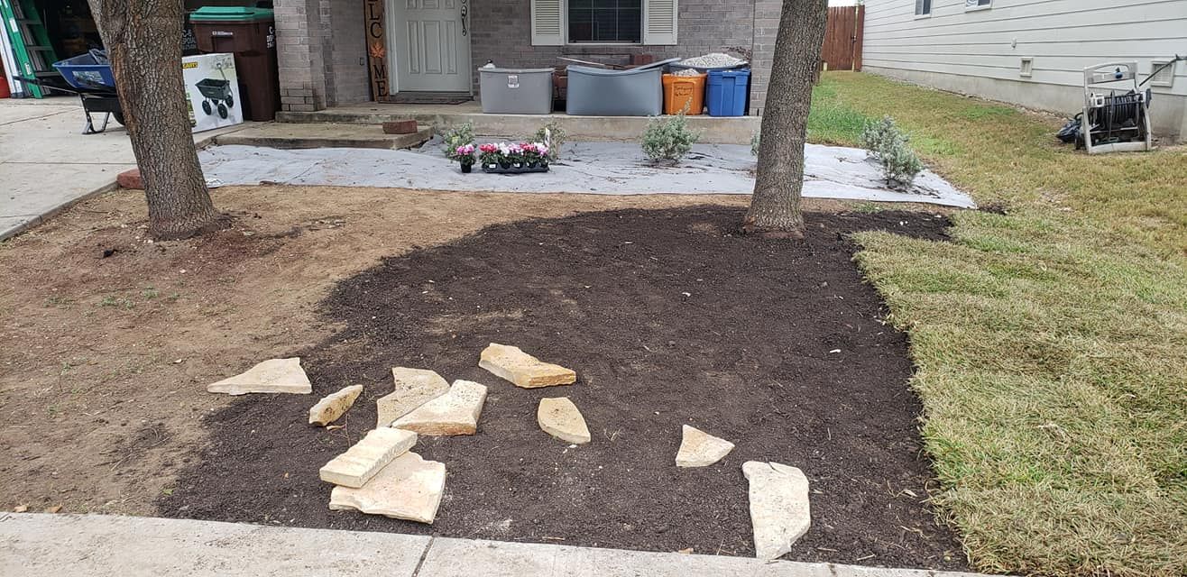 Freshly landscaped yard with dark soil and stepping stones in front of a house; trees and potted plants nearby
