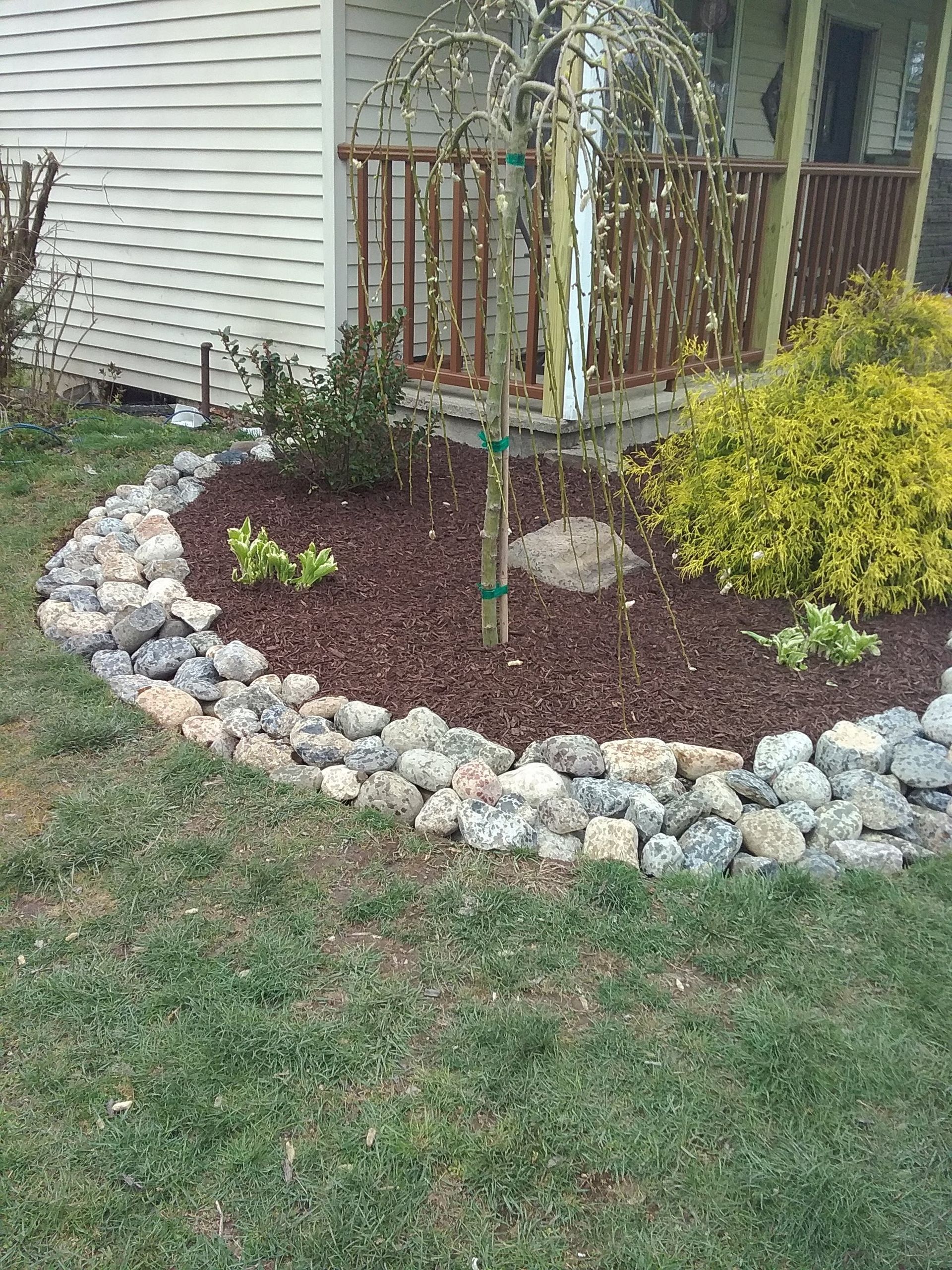 A garden with rocks and mulch in front of a house.