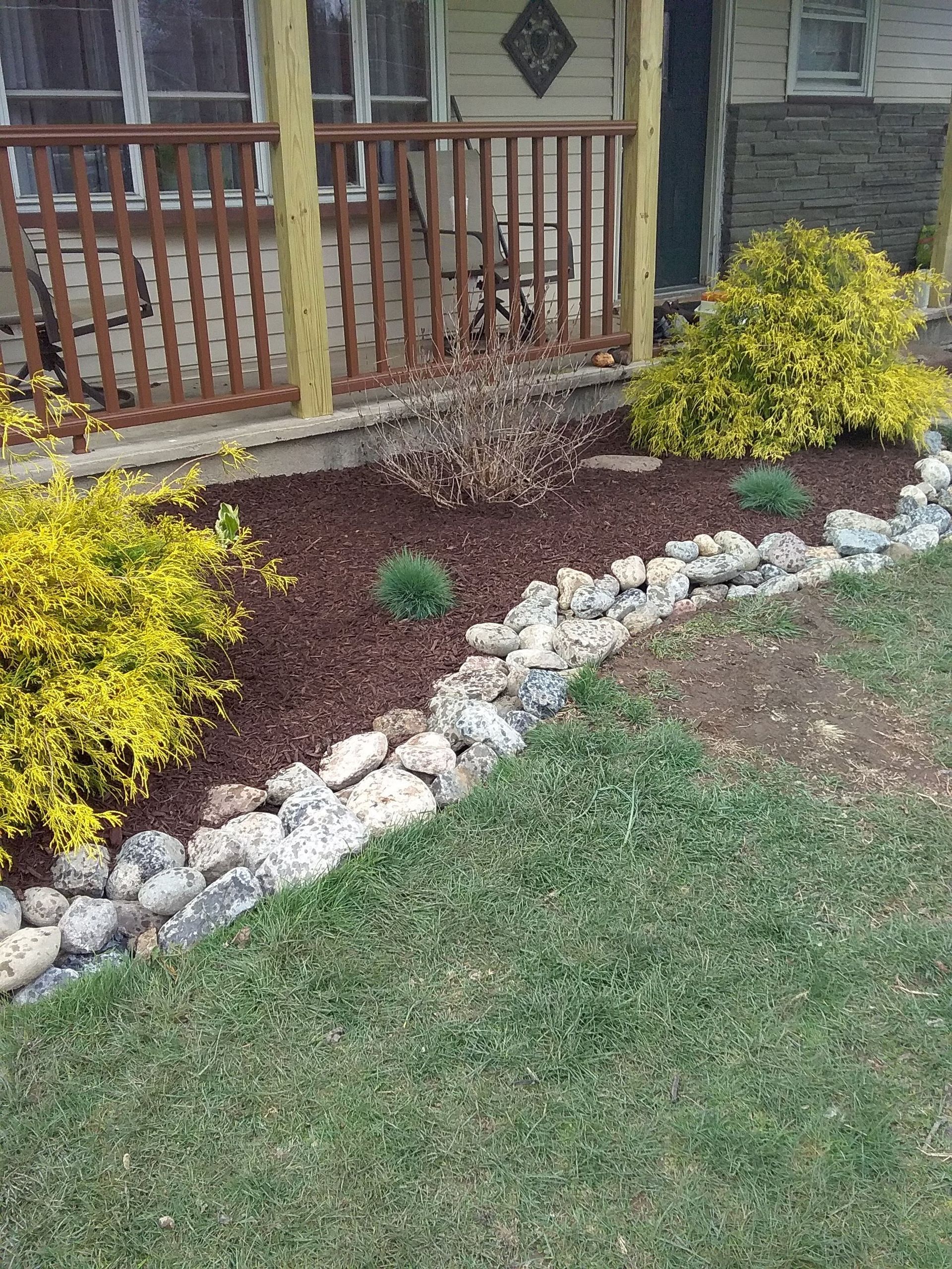 A lawn with rocks and plants in front of a house with a porch.