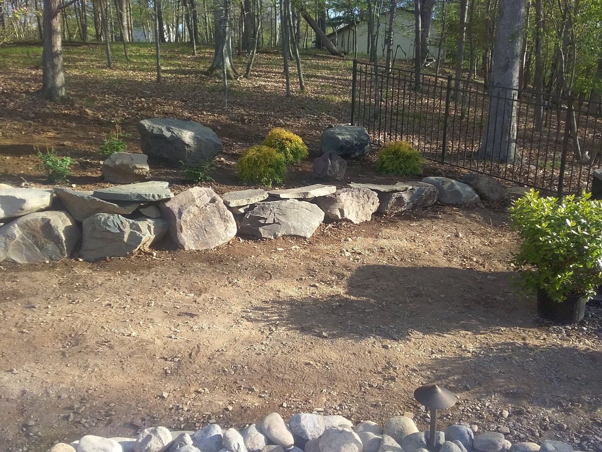a rock wall in a yard with trees in the background