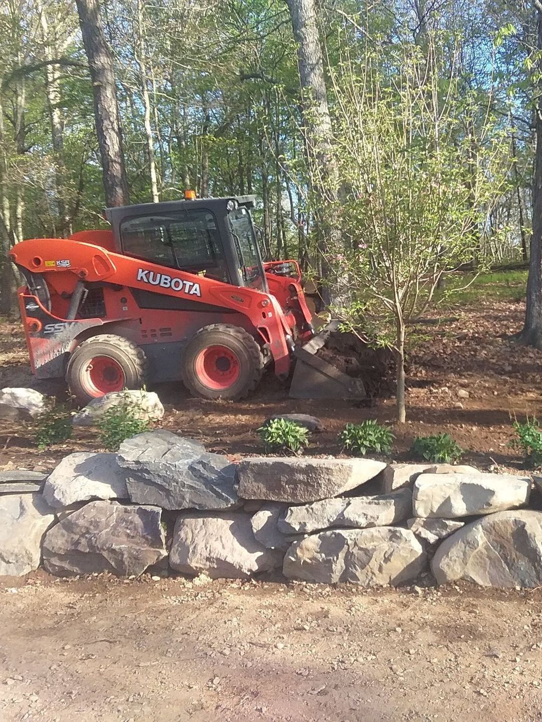 a red and black tractor is parked next to a rock wall .