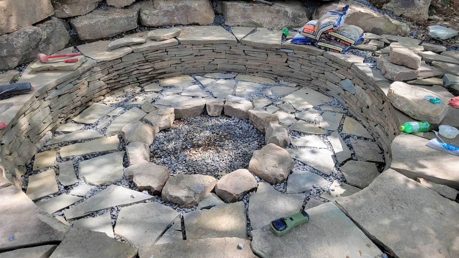 Stone fire pit with rock wall surround and stone floor, surrounded by rocks and a few toys.