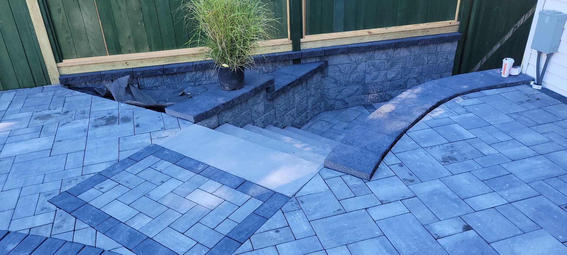 A brick patio with stairs and a green fence in the background.