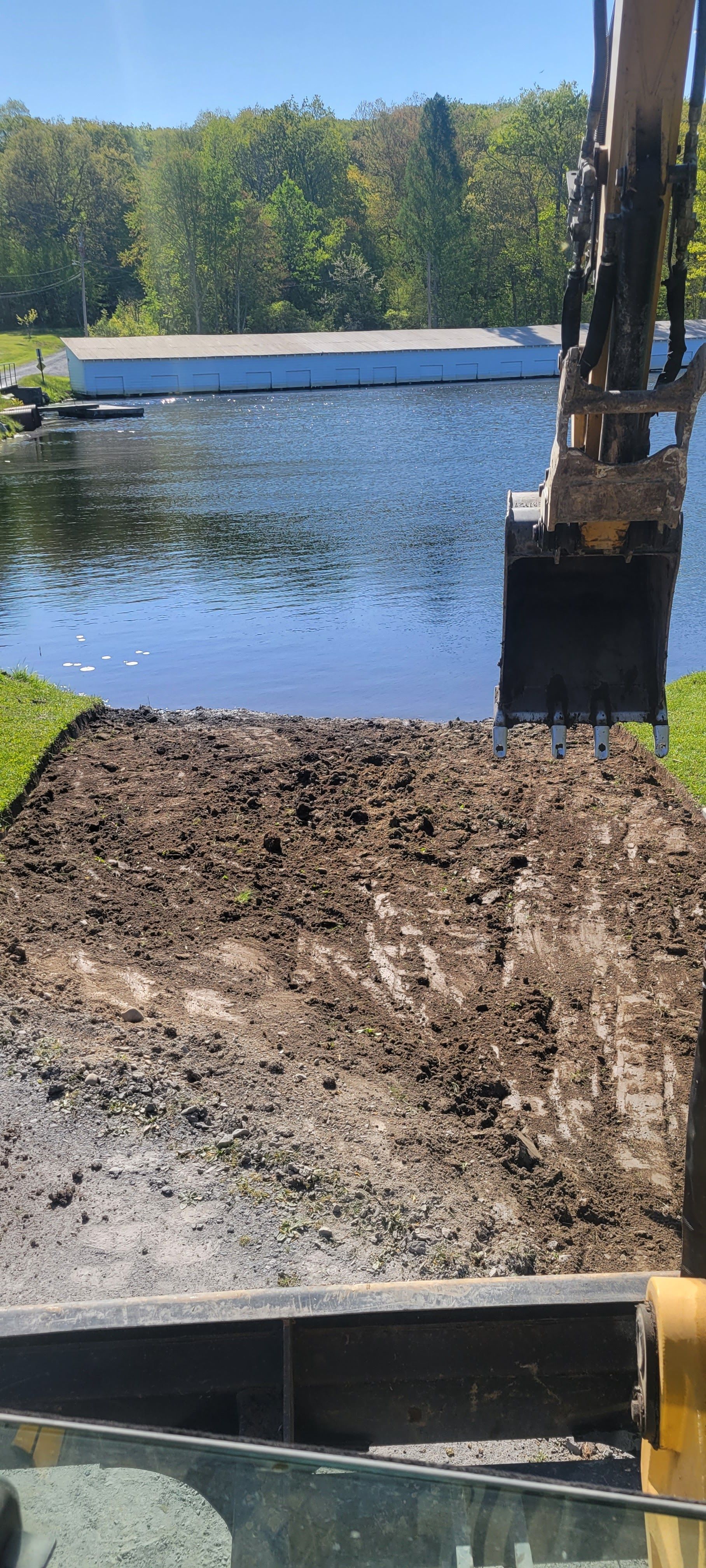 a large excavator is digging a hole in the ground next to a body of water .