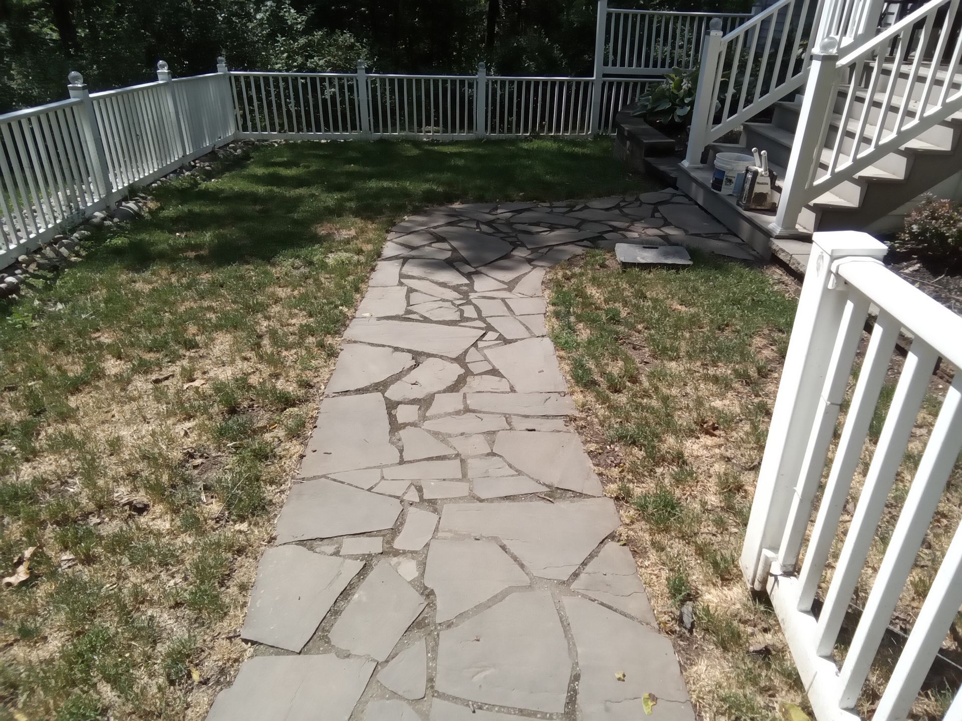Stone path through grass, bordered by white fence and stairs.
