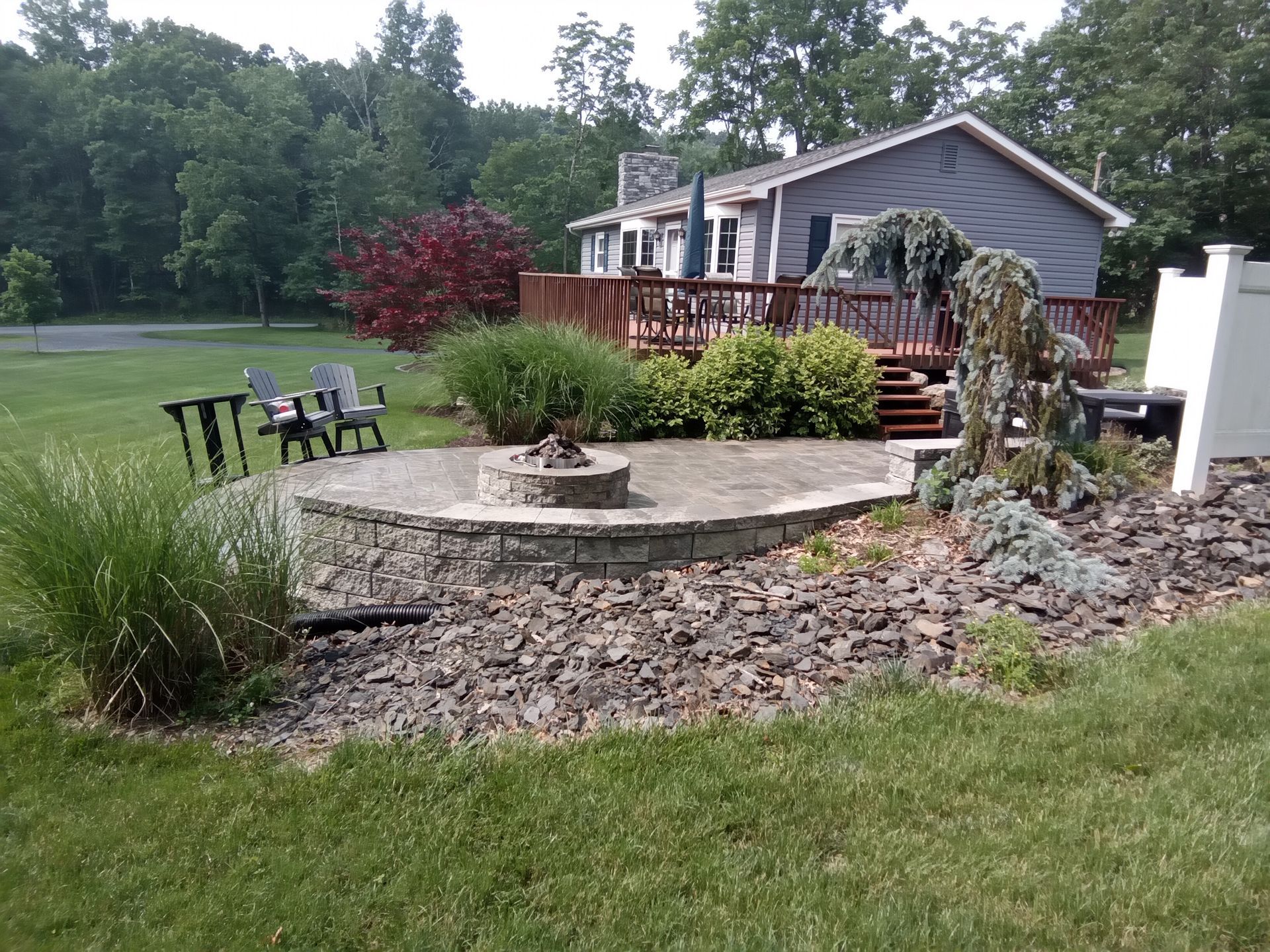 Backyard with a stone fire pit, deck, landscaping, and a house.