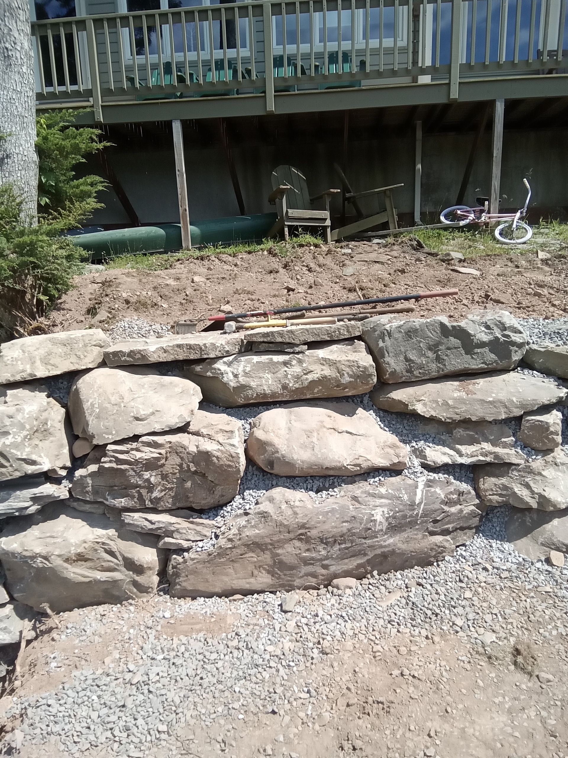 Stone retaining wall in front of a house, with gravel base.