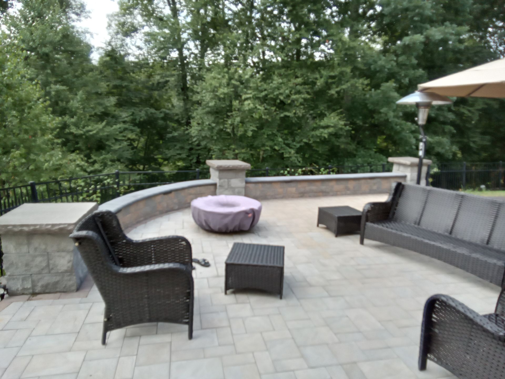 Patio with wicker furniture, fire pit, and stone wall overlooking trees.