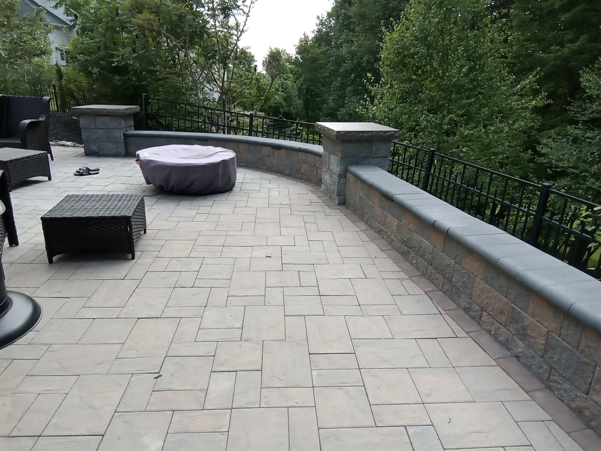 Patio with stone pavers, a fire pit under a cover, and a low wall with a black fence.