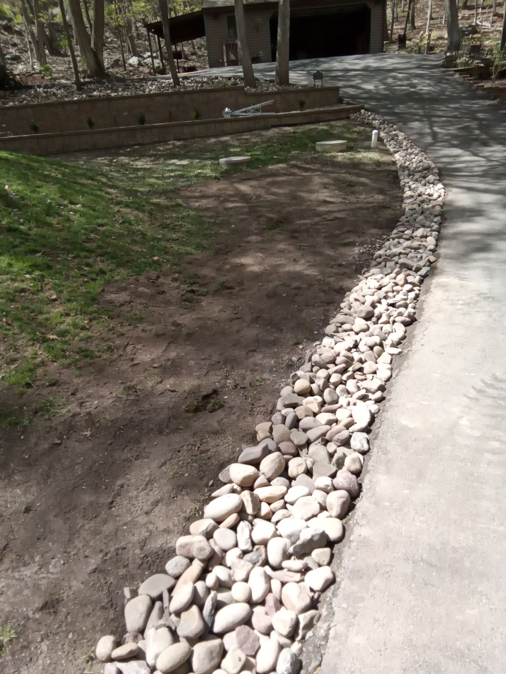 Rock border next to a concrete path and dirt area, with a building in the background.