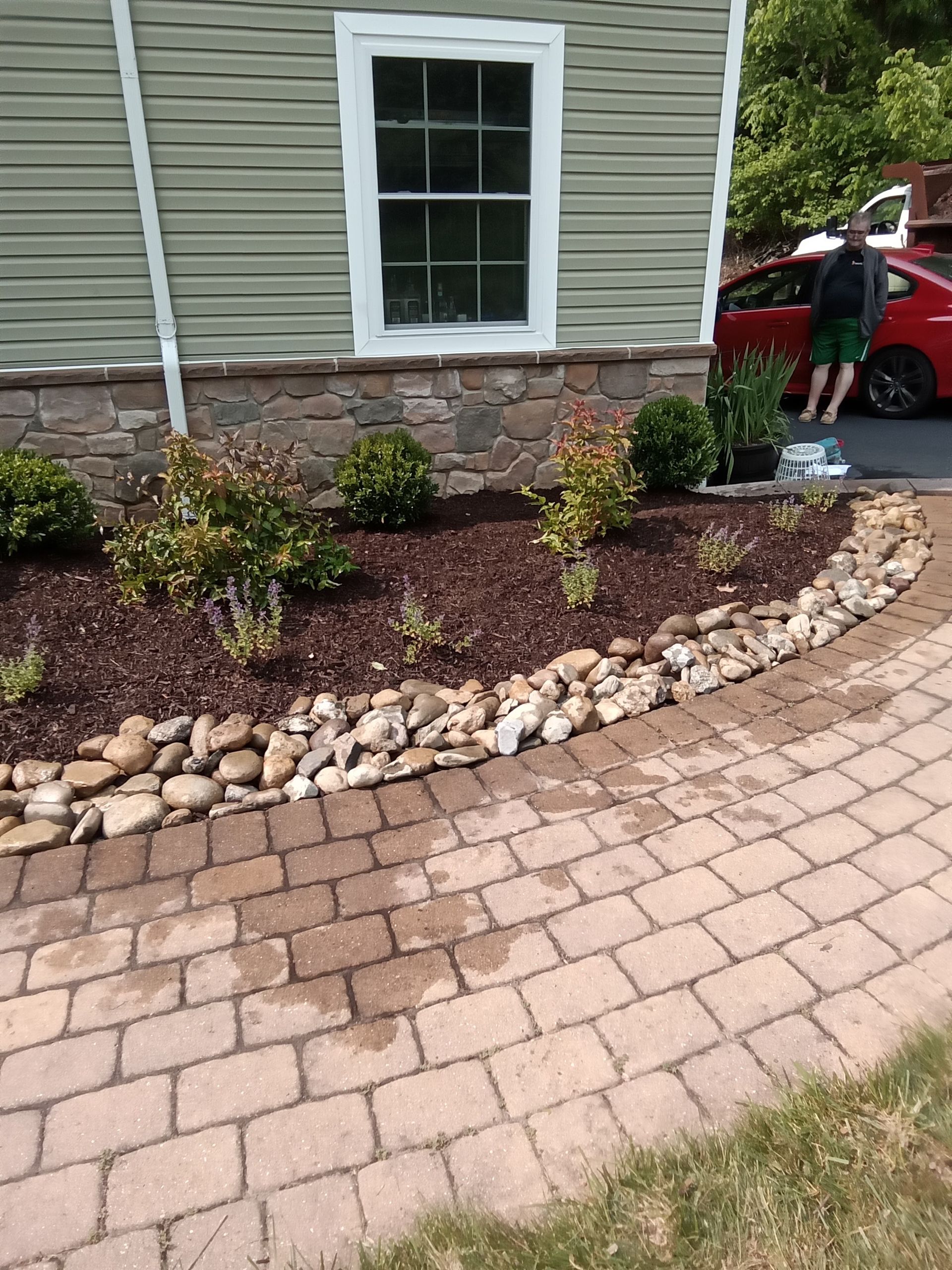 A house with a stone foundation, a flowerbed with rocks, and a brick walkway.