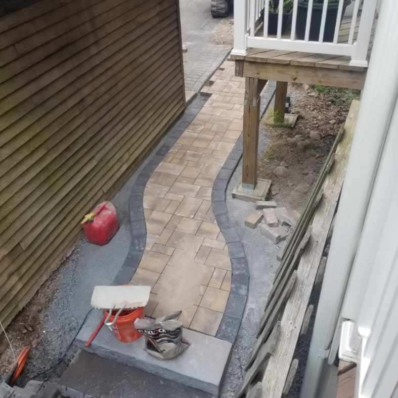 a brick walkway is being built by A.A.F Landscaping in the backyard of a house .