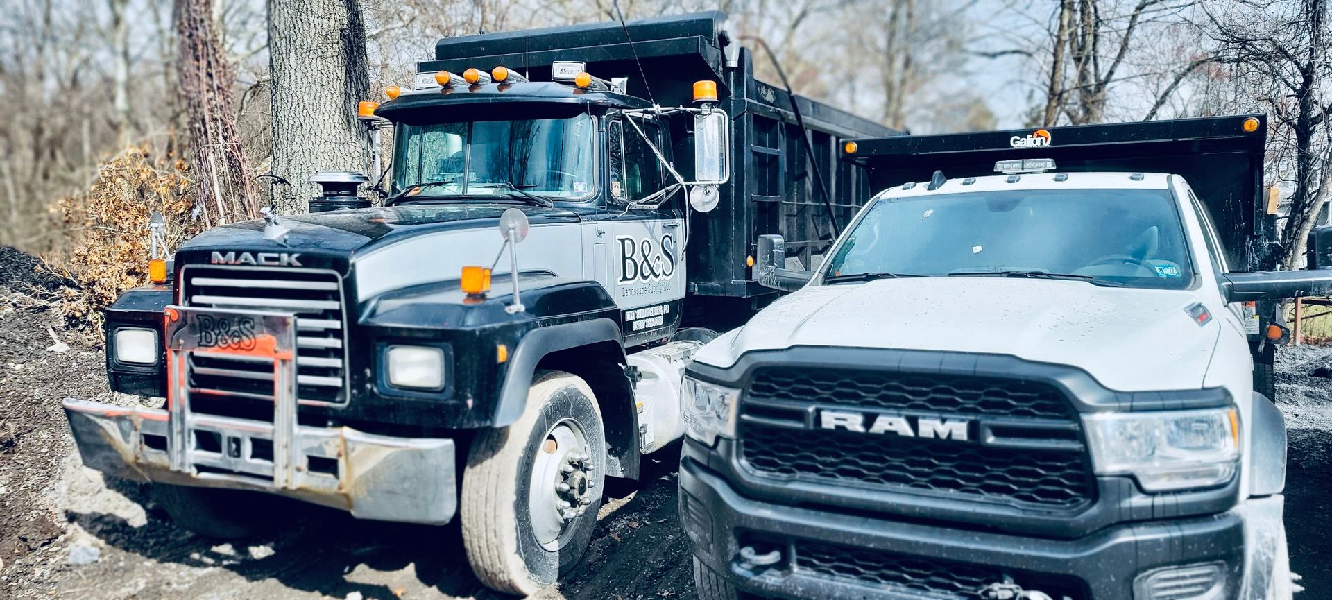 A.A.F Landscaping dump truck and a ram truck are parked next to each other on a dirt road .