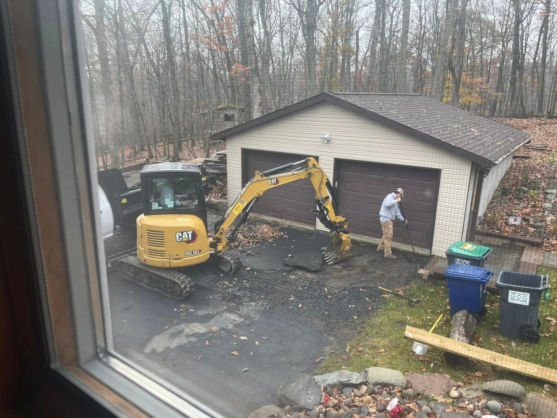 a man is standing next to a yellow excavator in front of a garage .