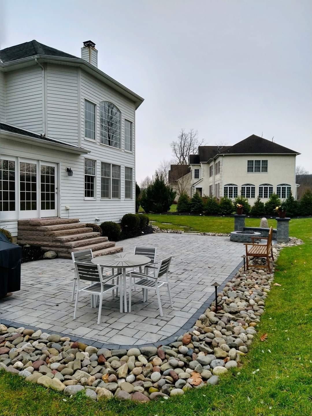 A patio with a table and chairs in front of a large white house.