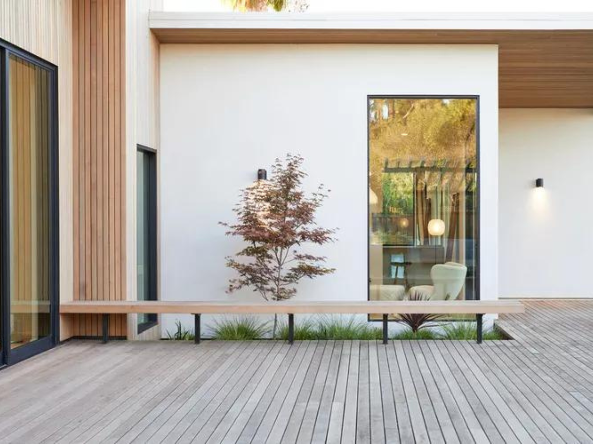 A white house with a wooden deck and a bench in front of it.