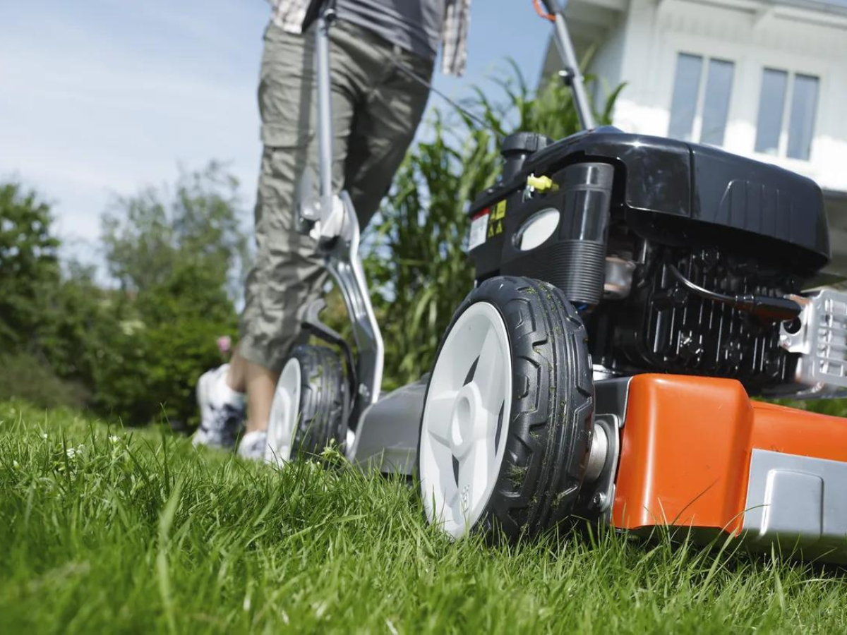 A person is using a lawn mower to cut the grass in front of a house.