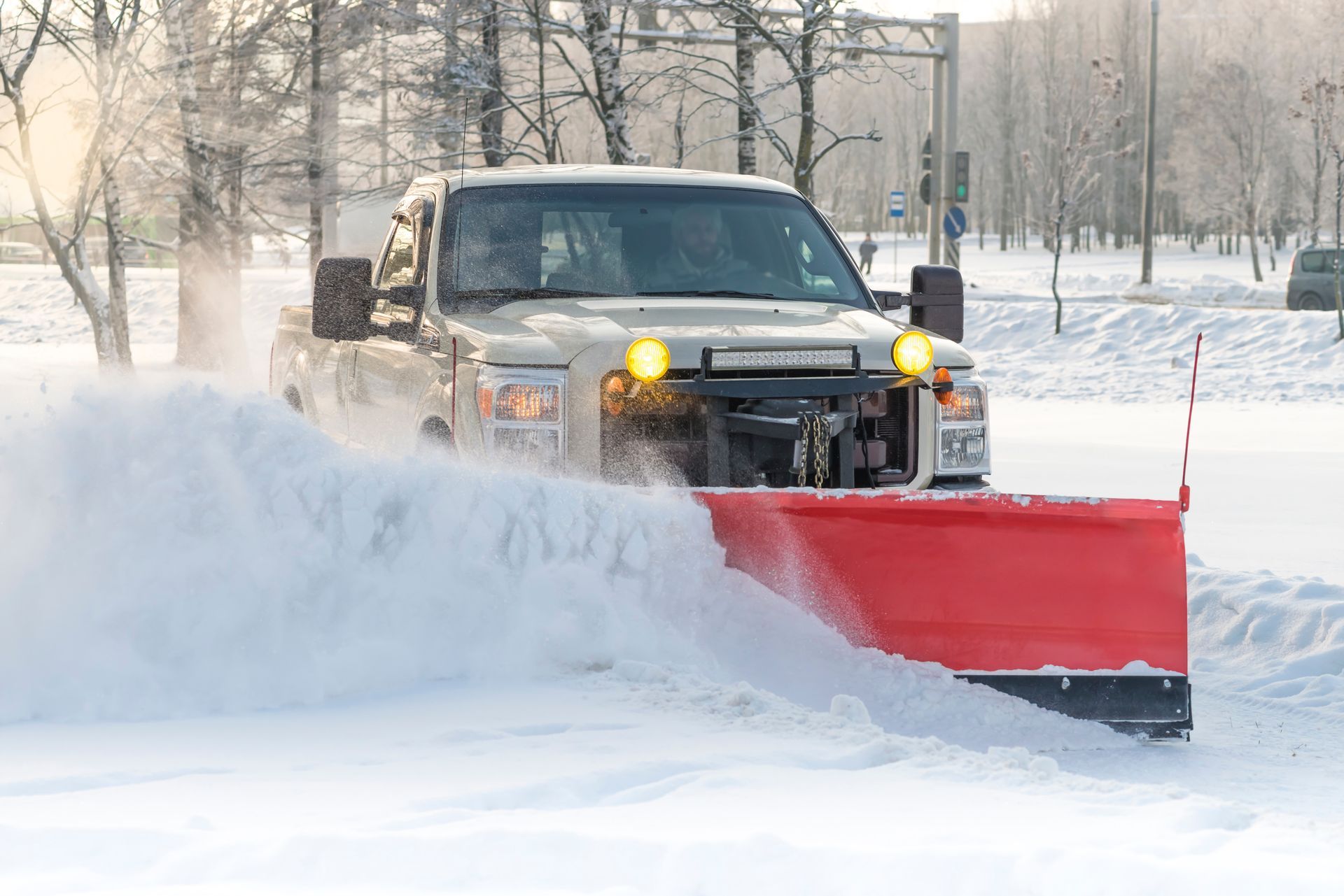 Snowplow truck clearing snow from a road, spraying snow outwards, on a sunny day.