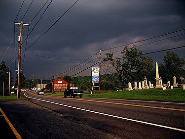 A car is driving down a road with a cemetery in the background