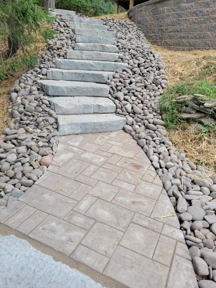 Stone steps ascend a gravel-lined hillside, leading from a textured concrete path.