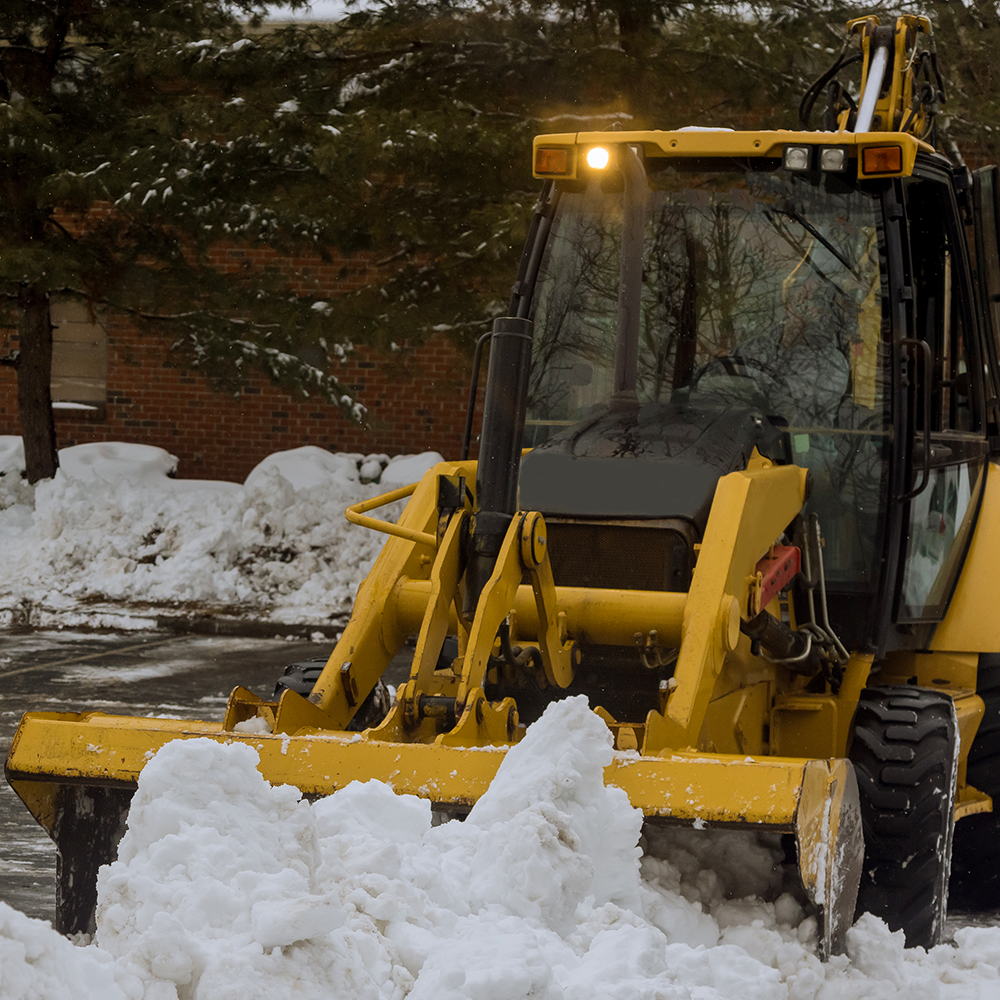 A yellow tractor is clearing snow from a parking lot